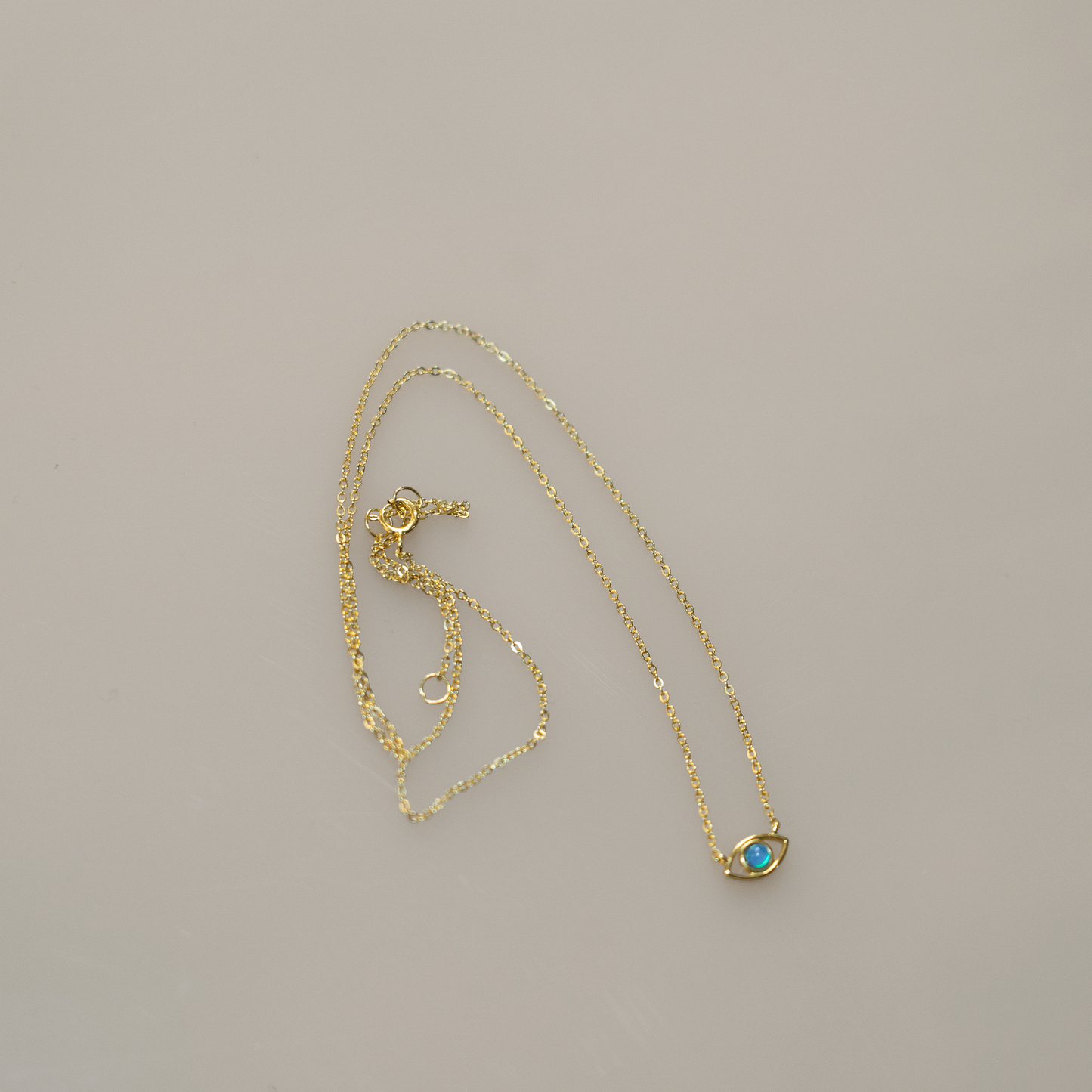 Gold vermeil chain with lobster clasp holds an evil eye charm. The eye is a round blue opal set in gold with a hanging gold vermeil chain below. Sterling silver and opal, gold-plated.