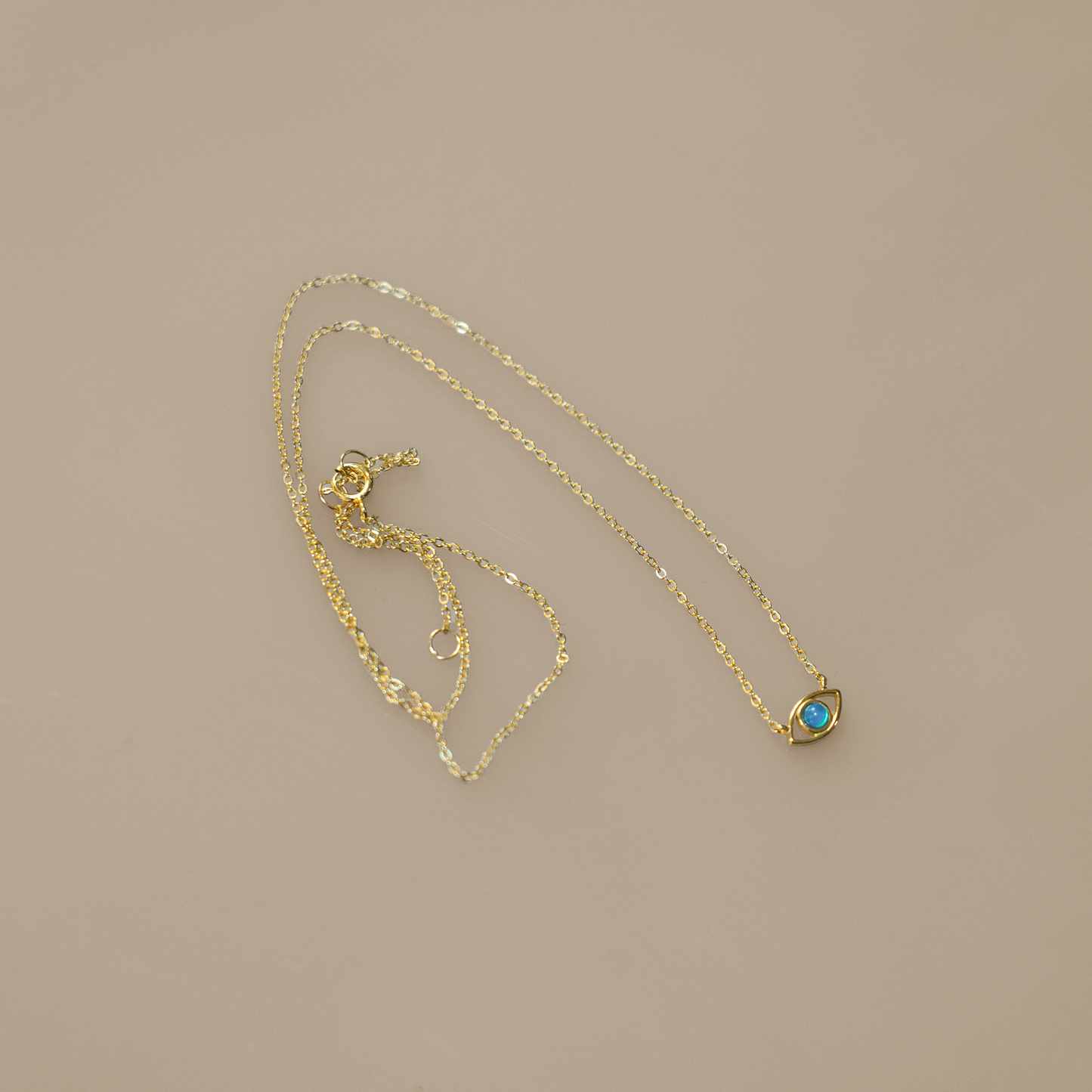 Gold vermeil chain with lobster clasp holds an evil eye charm. The eye is a round blue opal set in gold with a hanging gold vermeil chain below. Sterling silver and opal, gold-plated.