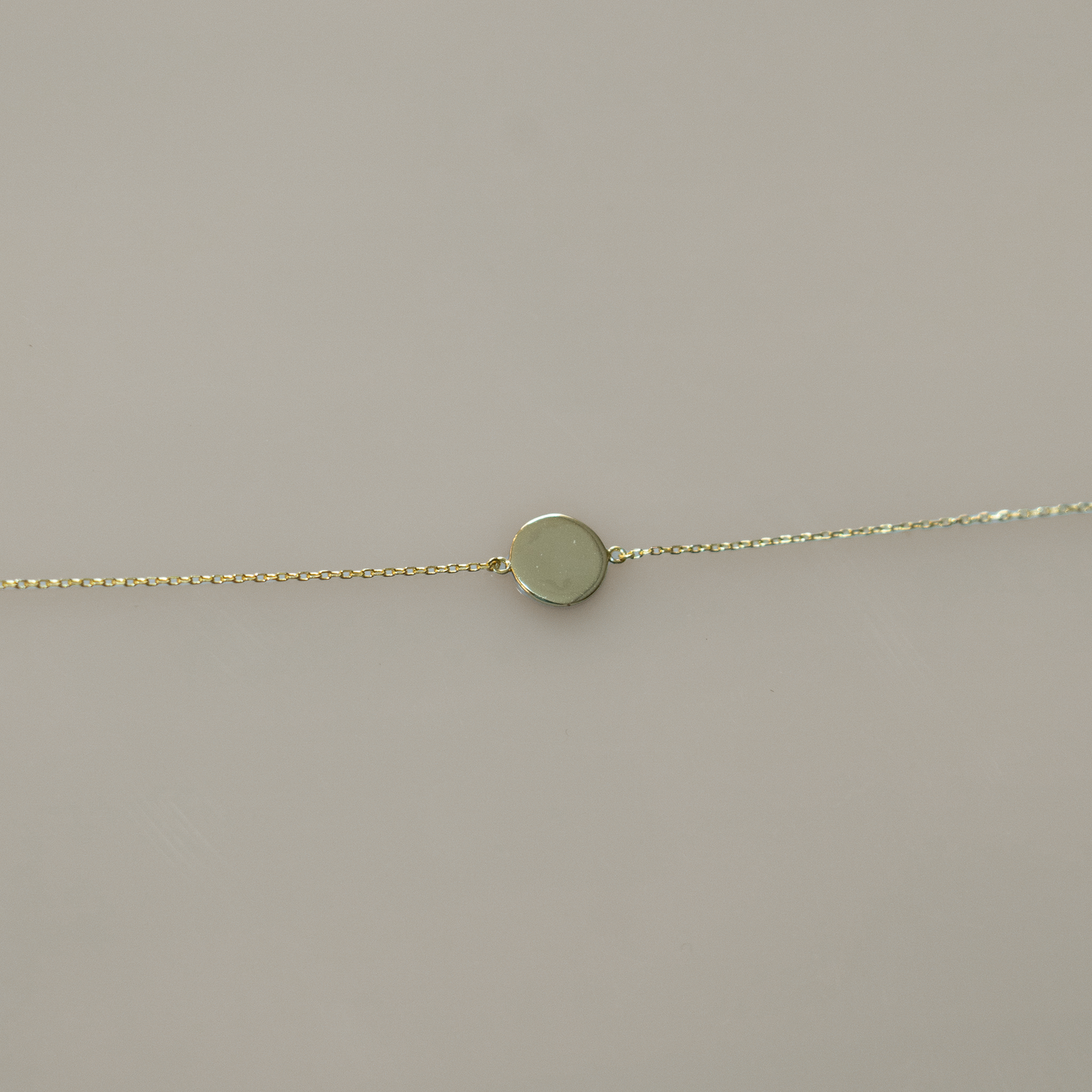 Delicate gold chain bracelet featuring a single, smooth, round coin charm. Perfect for layering with other bracelets or for a touch of minimalist elegance on its own.