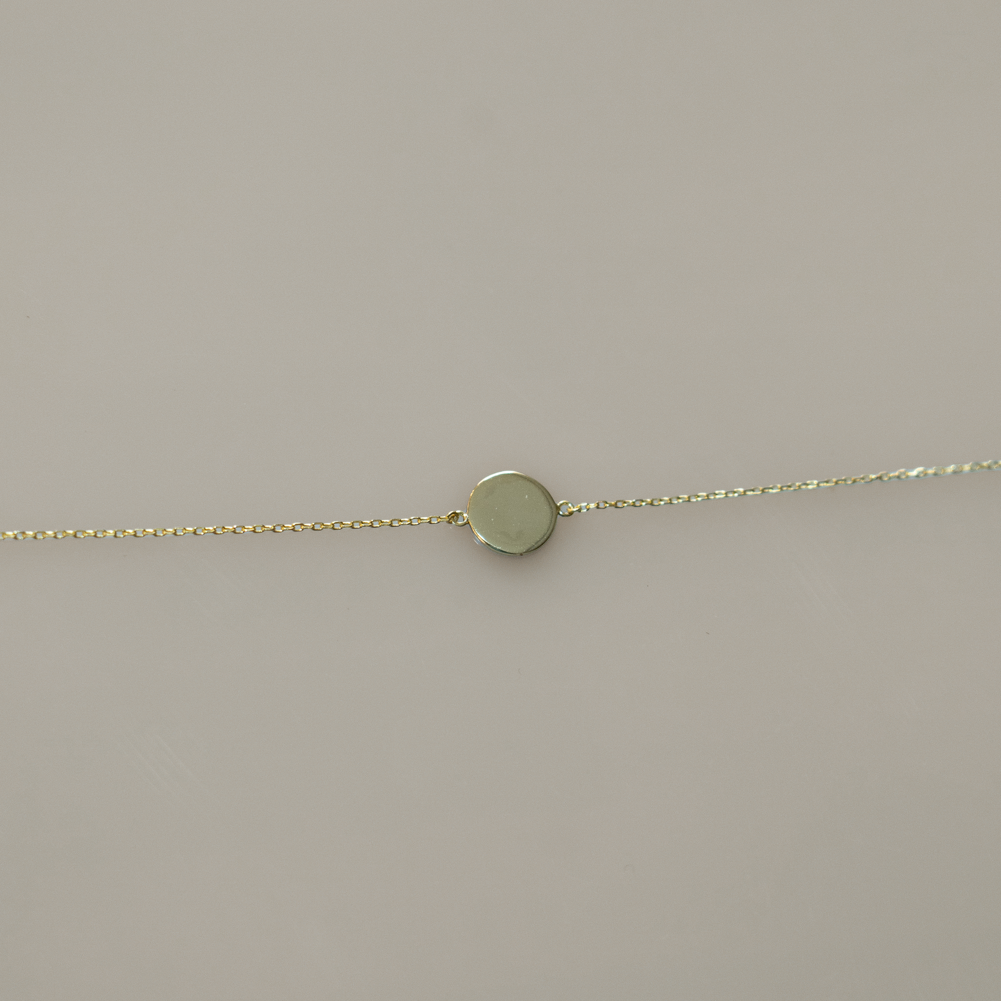 Delicate gold chain bracelet featuring a single, smooth, round coin charm. Perfect for layering with other bracelets or for a touch of minimalist elegance on its own.