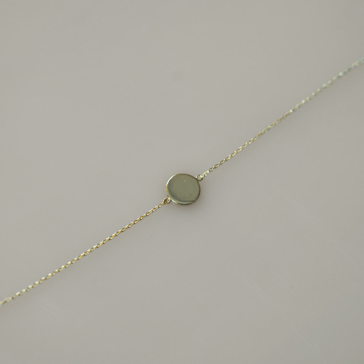 Delicate gold chain bracelet featuring a single, smooth, round coin charm. Perfect for layering with other bracelets or for a touch of minimalist elegance on its own.