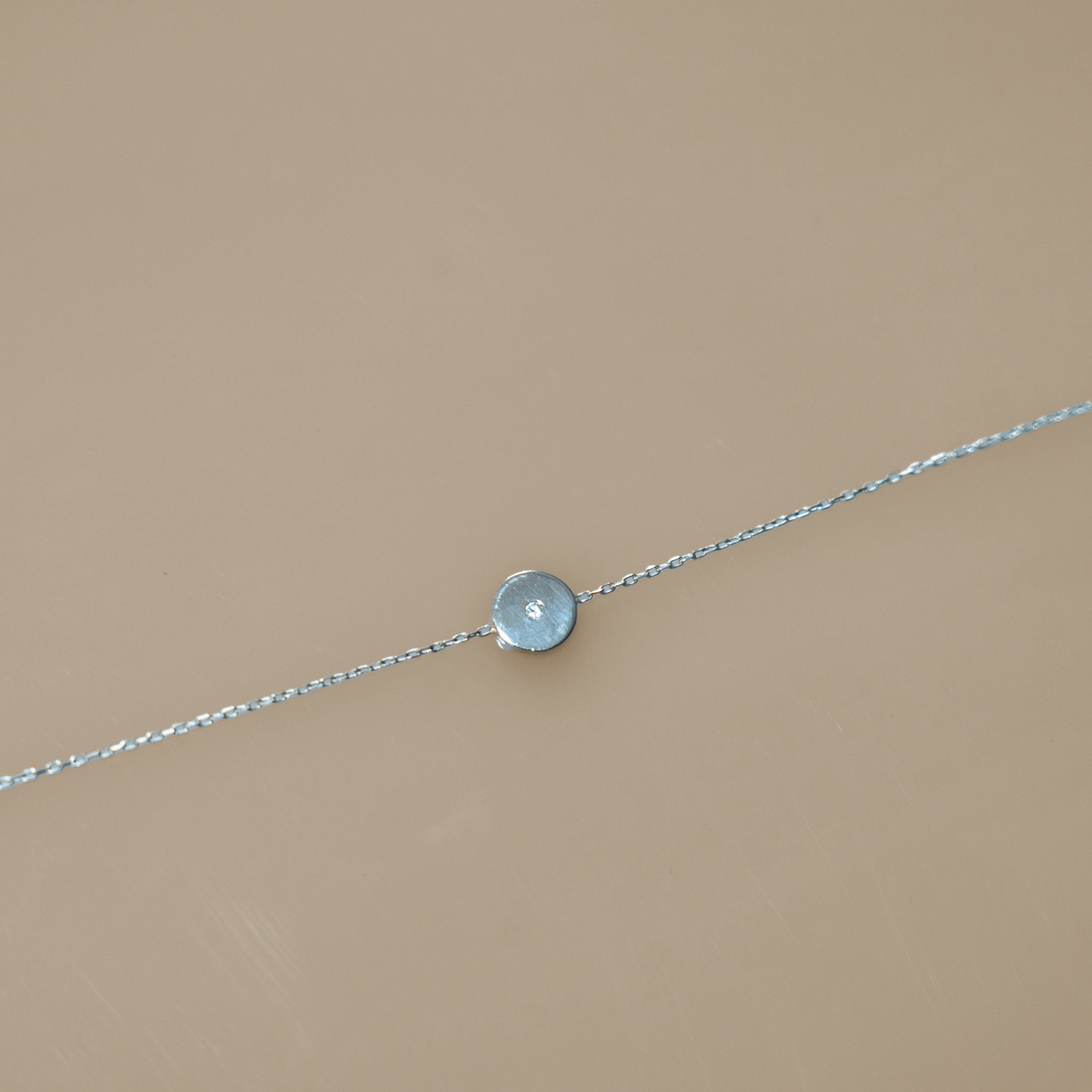 Delicate silver chain bracelet featuring a single, smooth, round coin charm. Perfect for layering with other bracelets or for a touch of minimalist elegance on its own.