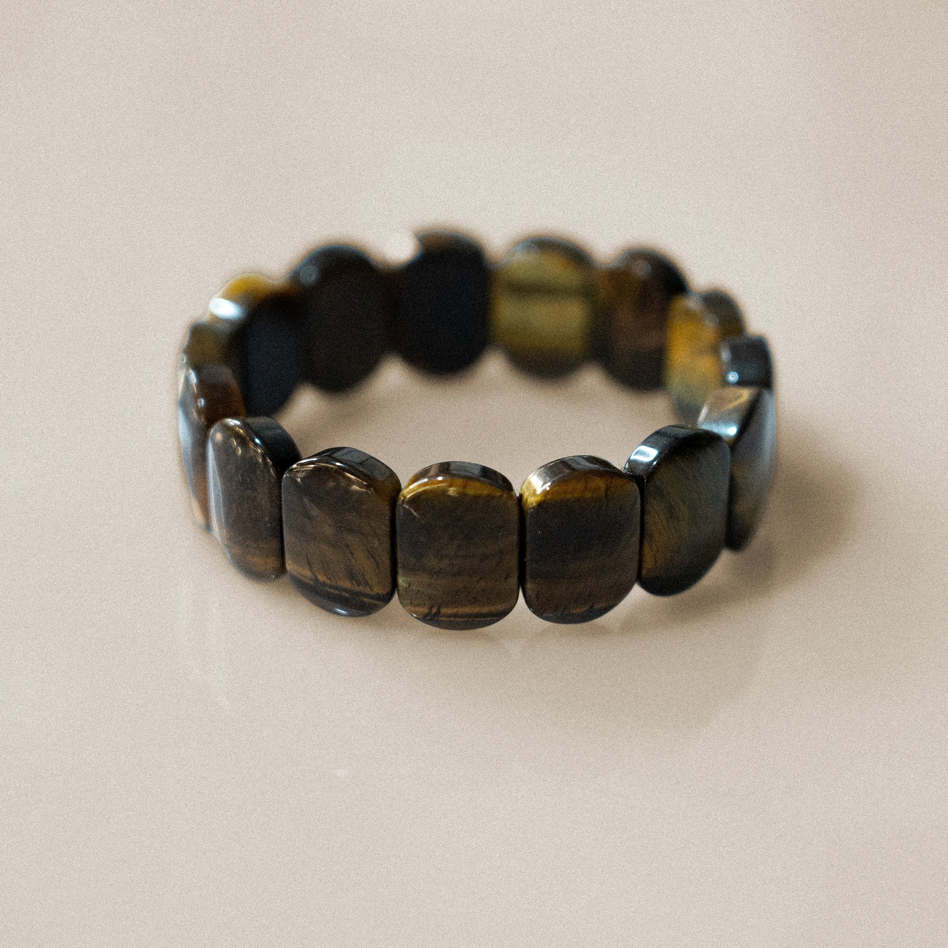 The bracelet consists of rectangular tigers eye stones, arranged side by side to form a continuous band. It has no visible closure, likely elastic. The stones are glossy, displaying rich brown and golden hues. The material is tigers eye.