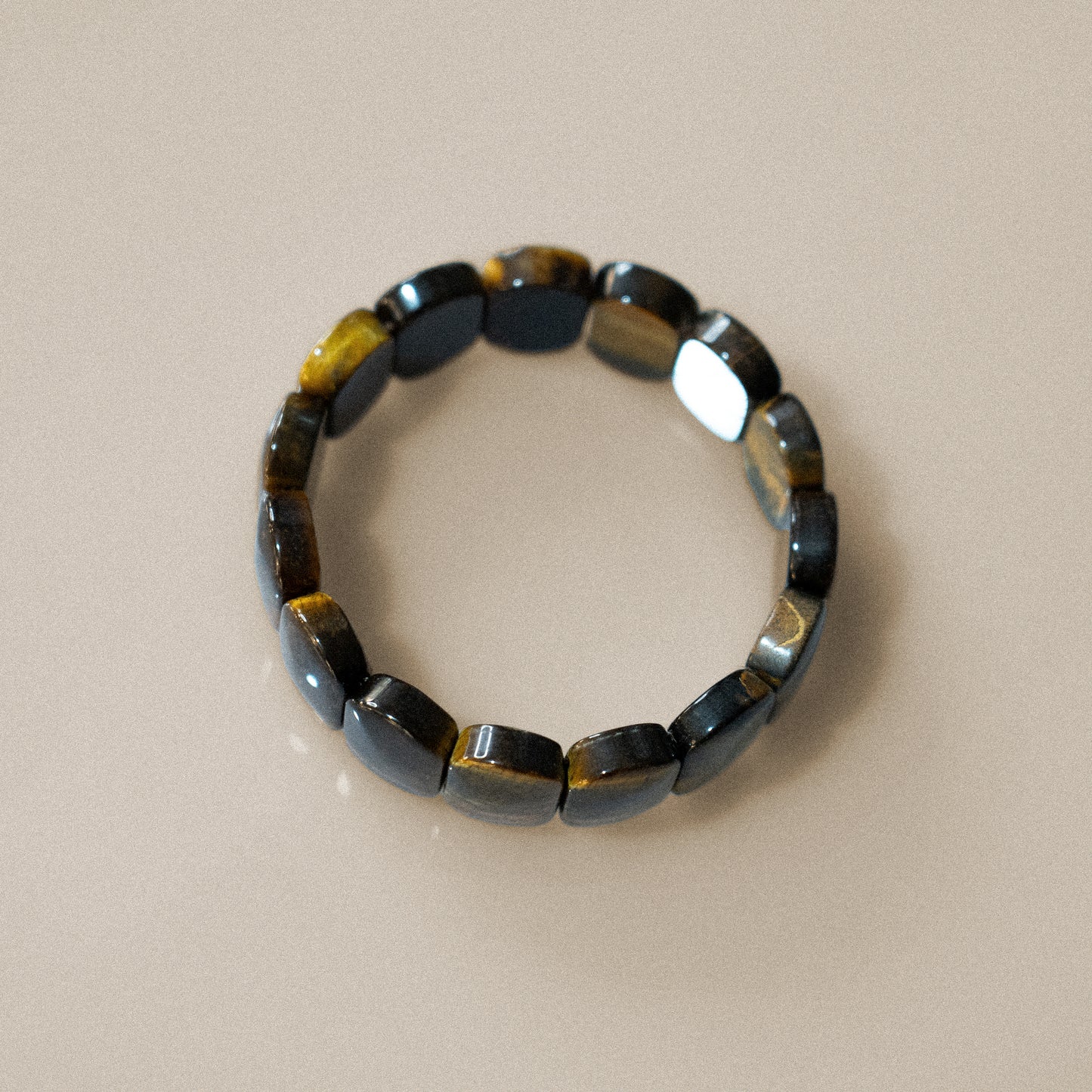 The bracelet consists of rectangular tigers eye stones, arranged side by side to form a continuous band. It has no visible closure, likely elastic. The stones are glossy, displaying rich brown and golden hues. The material is tigers eye.