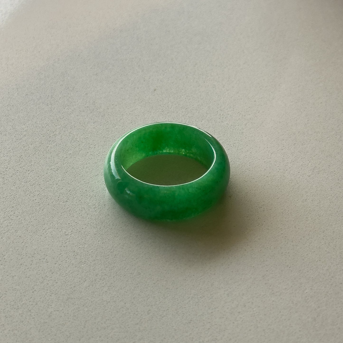 The image depicts a smooth, rounded, bright green jade ring. It has a simple, sleek circular band shape, appearing to be carved from a single piece of jade with no visible setting or stones.