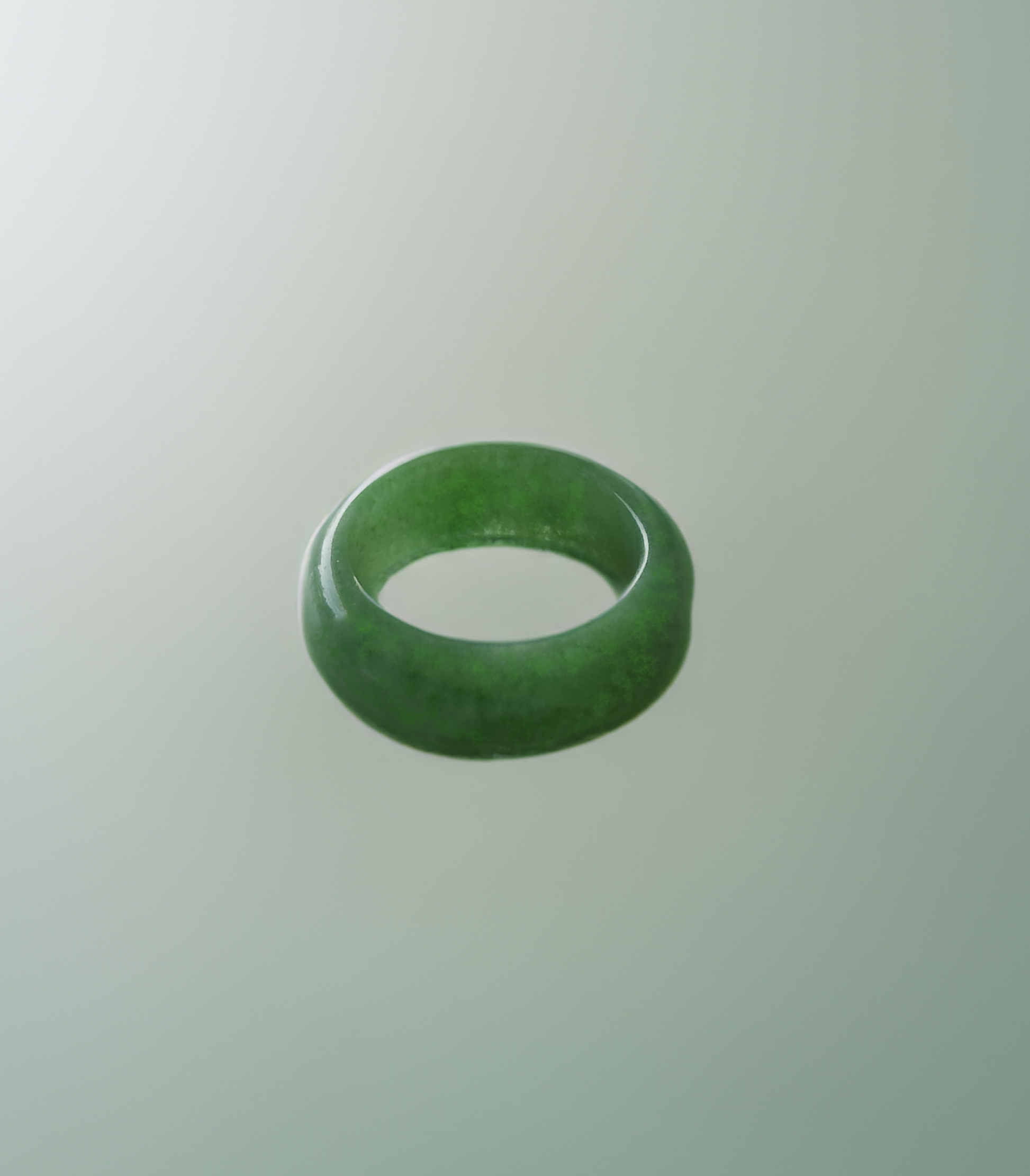 The image depicts a smooth, rounded, bright green jade ring. It has a simple, sleek circular band shape, appearing to be carved from a single piece of jade with no visible setting or stones.