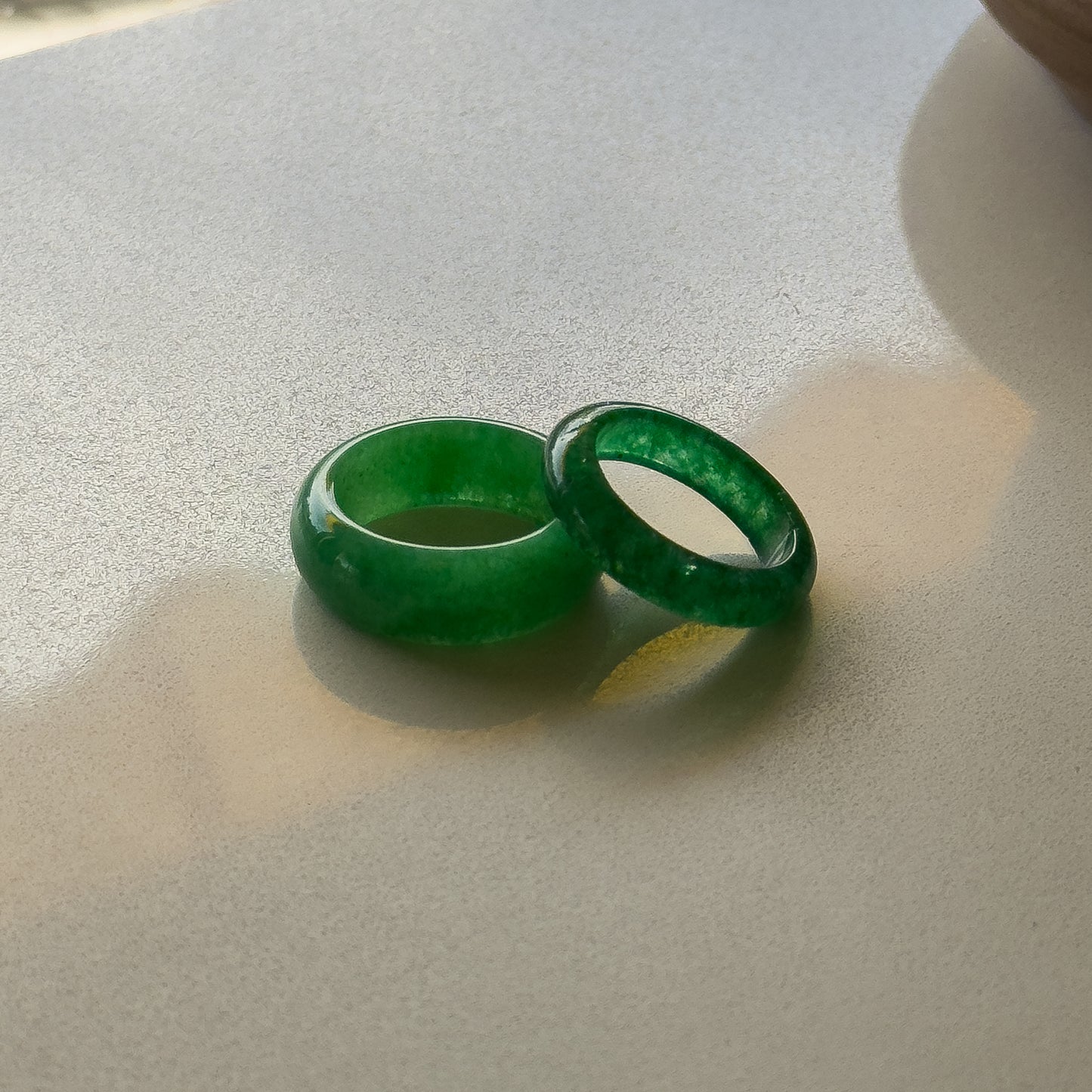 The image depicts a smooth, rounded, bright green jade ring. It has a simple, sleek circular band shape, appearing to be carved from a single piece of jade with no visible setting or stones.