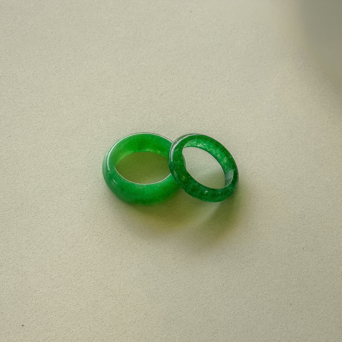 The image depicts a smooth, rounded, bright green jade ring. It has a simple, sleek circular band shape, appearing to be carved from a single piece of jade with no visible setting or stones.