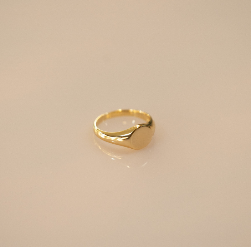 The ring forms a simple, circular shape that elegantly wraps around the finger. The sterling silver band is coated in a warm, golden layer of vermeil, giving it a timeless look reminiscent of classic Roman medallion designs.