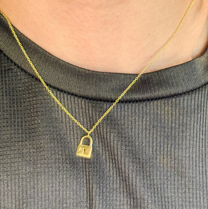 The necklace features a delicate gold vermeil chain, holding a small padlock-shaped pendant. The padlock is smooth and rectangular with rounded edges, made of sterling silver, coated in gold vermeil. The chain has a simple spring-ring closure.