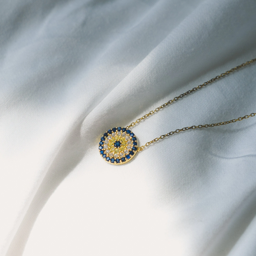 Round evil eye pendant necklace, 12mm diameter, crafted in 18k gold vermeil (thick gold layer over sterling silver). Blue and white cubic zirconia stones set in pendant. Adjustable chain length from 15 to 17 inches. Lobster claw clasp closure.