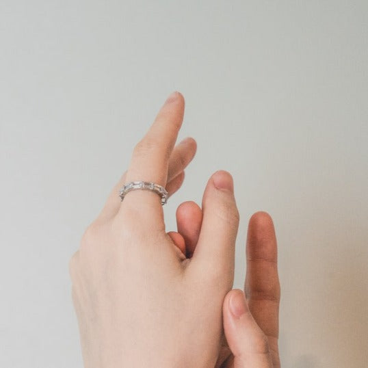 The image shows a ring featuring a row of rectangular-shaped diamonds or diamond-like stones set in a band of silver or platinum-toned metal. The setting appears to be a prong setting, securely holding the stones in place.