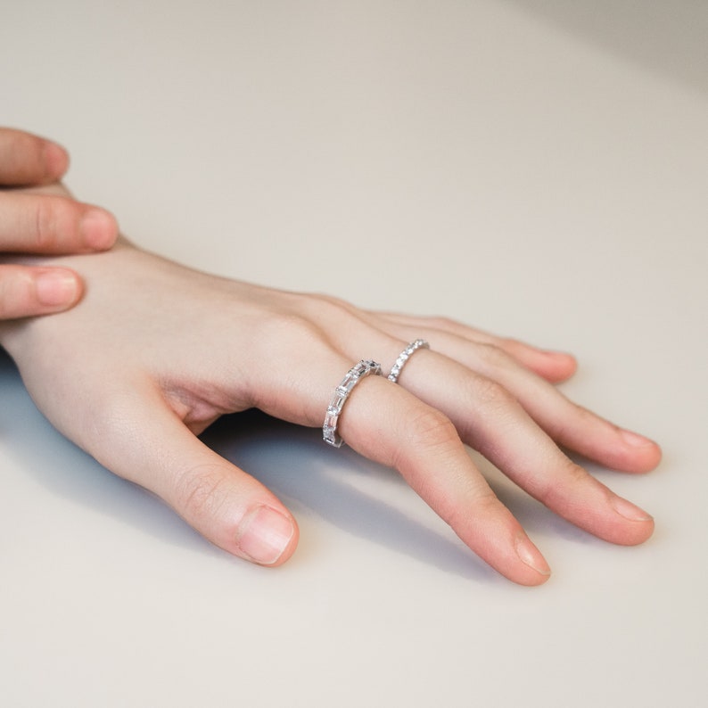 The image shows a ring featuring a row of rectangular-shaped diamonds or diamond-like stones set in a band of silver or platinum-toned metal. The setting appears to be a prong setting, securely holding the stones in place.