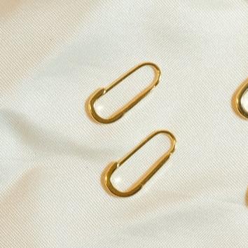 These earrings feature a simple, elongated paperclip design in gleaming 18k gold vermeil. The smooth, curved shape forms a delicate open hoop that hooks directly into the earlobe, embodying minimalist chic.