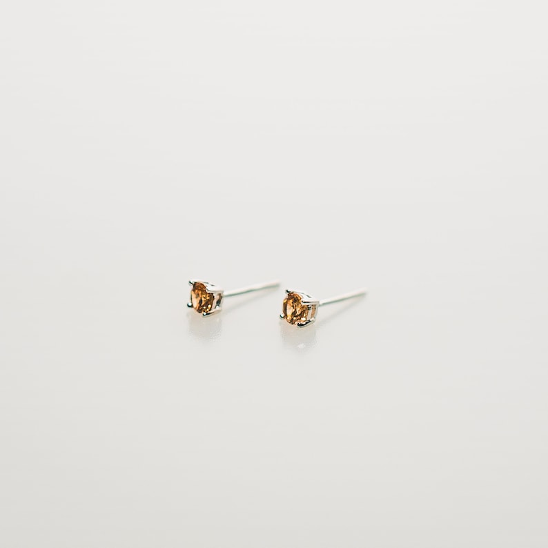 These earrings feature small, square-cut topaz gemstone set in sleek sterling silver studs. The minimalist design complements various ear piercings, from cartilage to lobes.