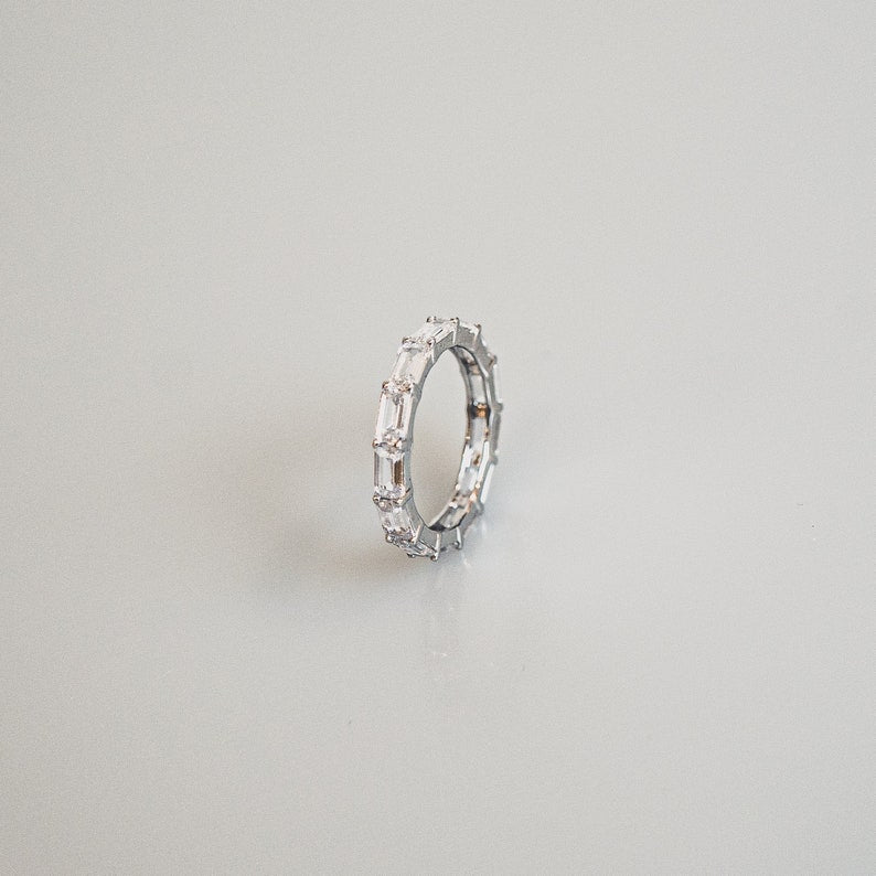 The image shows a ring featuring a row of rectangular-shaped diamonds or diamond-like stones set in a band of silver or platinum-toned metal. The setting appears to be a prong setting, securely holding the stones in place.