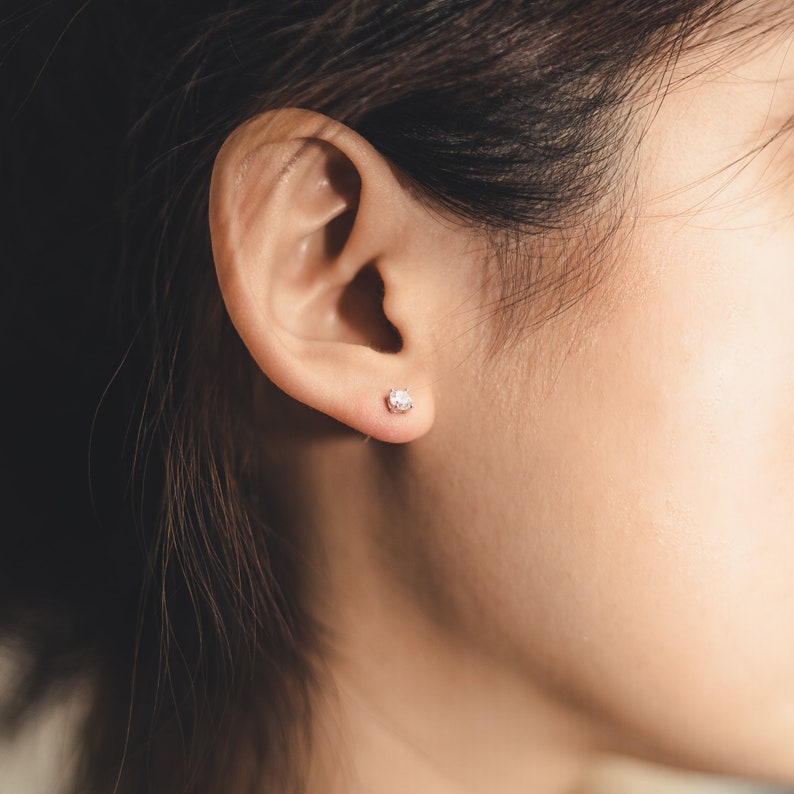 These earrings feature small, square-cut clear gemstone cubic zirconia, set in sleek sterling silver studs. The minimalist design complements various ear piercings, from cartilage to lobes.