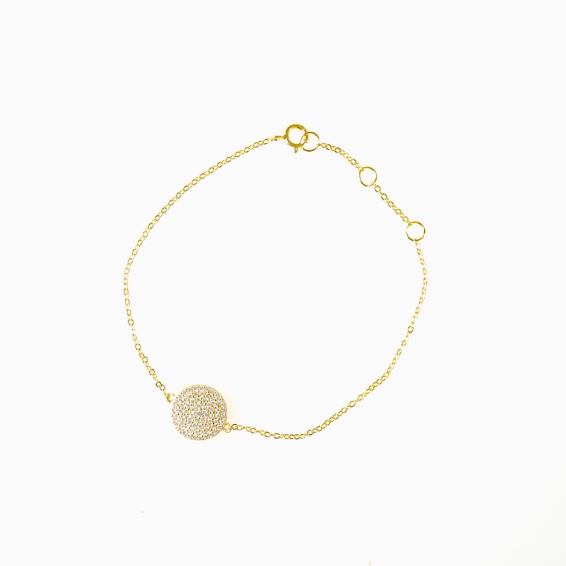 Delicate chain bracelet with small circular evil eye charm. Charm made of cubic zirconia set in 18k gold vermeil or sterling silver, measuring 10mm. Adjustable sliding bead closure allows 6 inc length. Shiny gold tones. Lightweight feel.