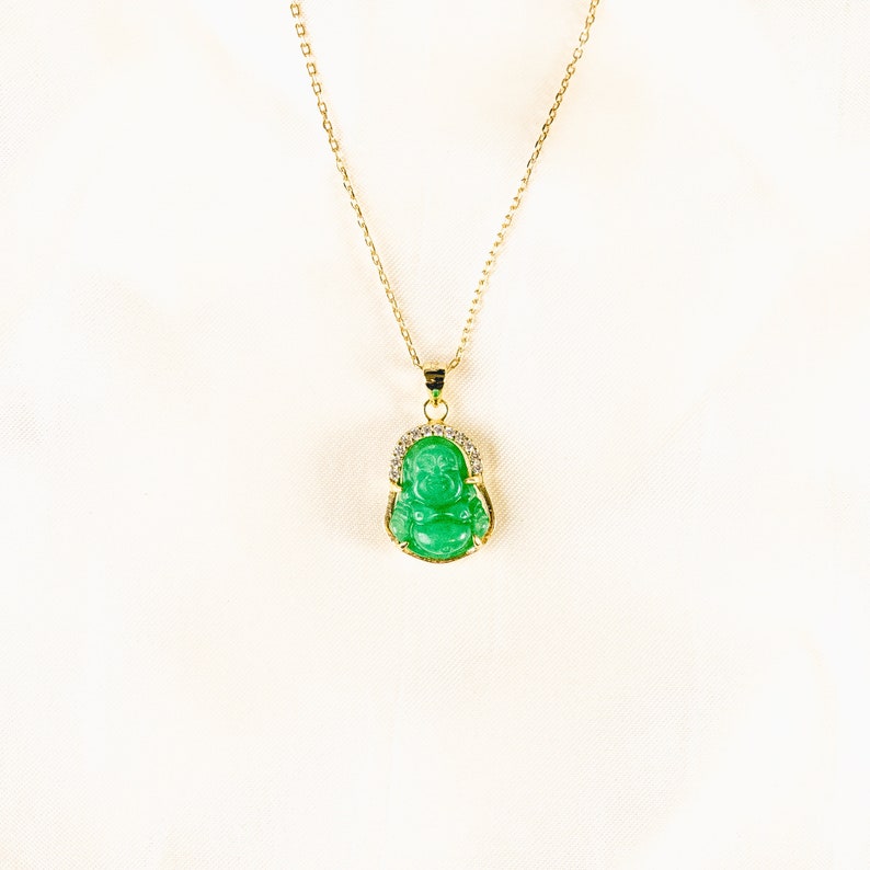 Pendant necklace featuring a small, 3D carved jade Buddha charm. Vibrant green jade stone set in 18k gold vermeil. Thin, adjustable gold vermeil cable chain, 16-18&quot; long with lobster clasp closure. Delicate and lightweight.