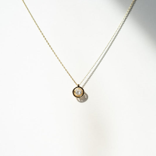 Round pendant necklace. Gold bezel set clear stone on silver chain bathed in gold vermeil. Pendant 8mm wide. Lobster clasp closure. Made of gold vermeil over sterling silver with cubic zirconia stone.